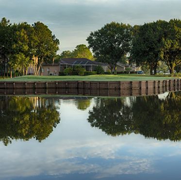 A reflection of trees in a body of water with a house in the background.