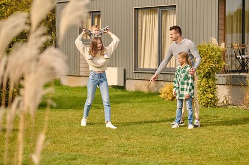 Family playing in a grassy yard outside a house, with a child and two adults smiling.