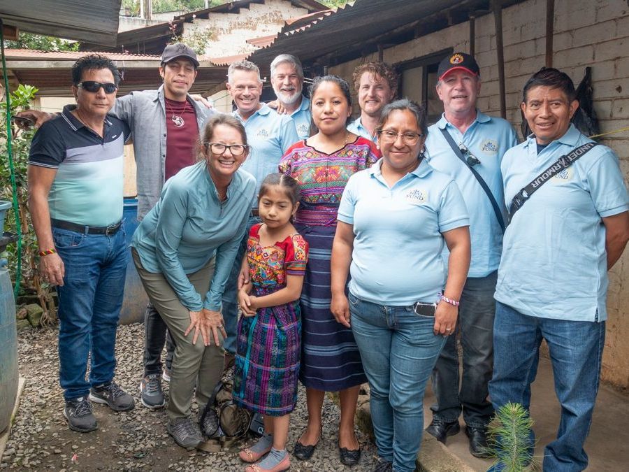 Group of diverse people smiling outdoors, some wearing light blue shirts.