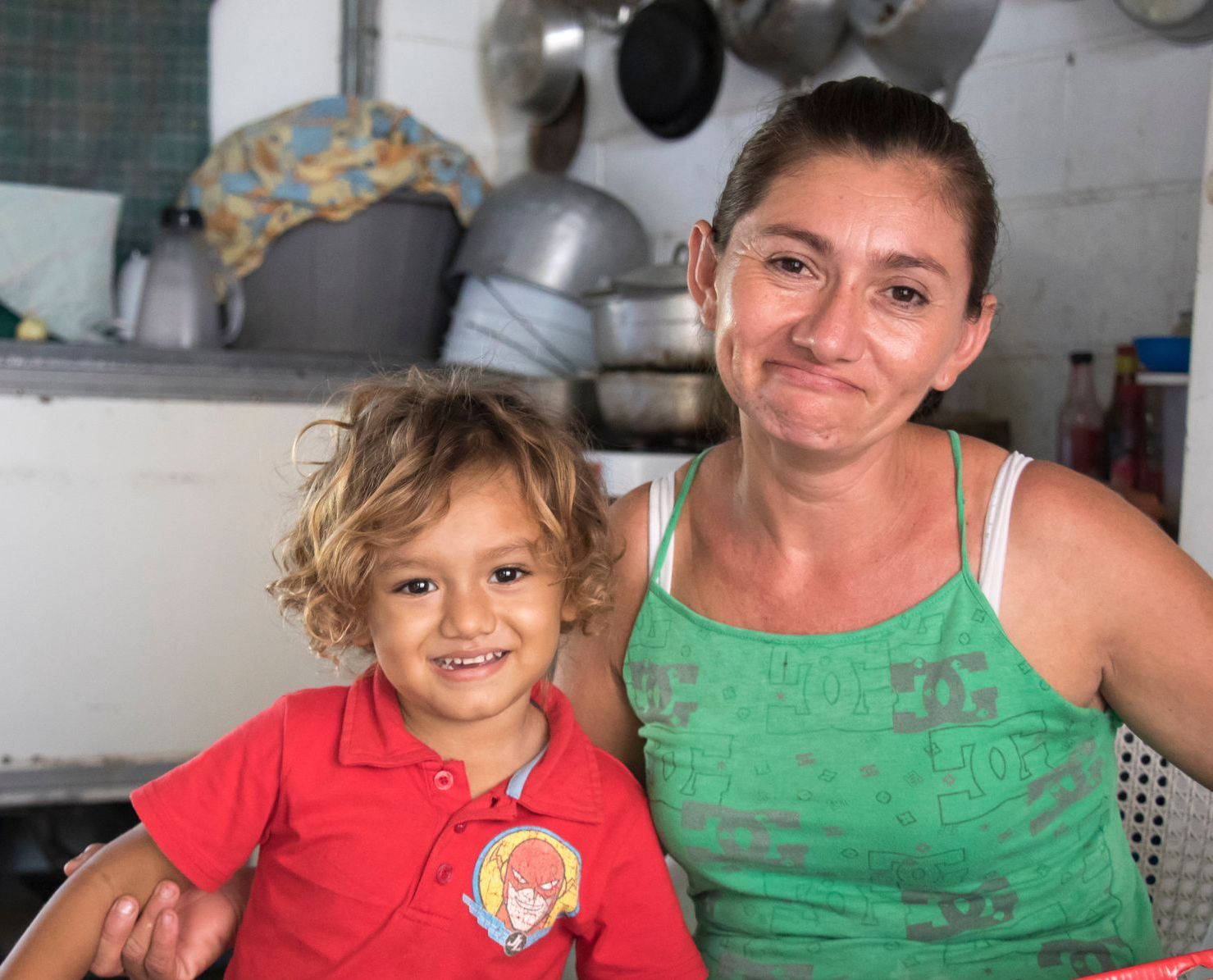 Woman and child smiling in a kitchen. The woman is wearing green, the child is in red.