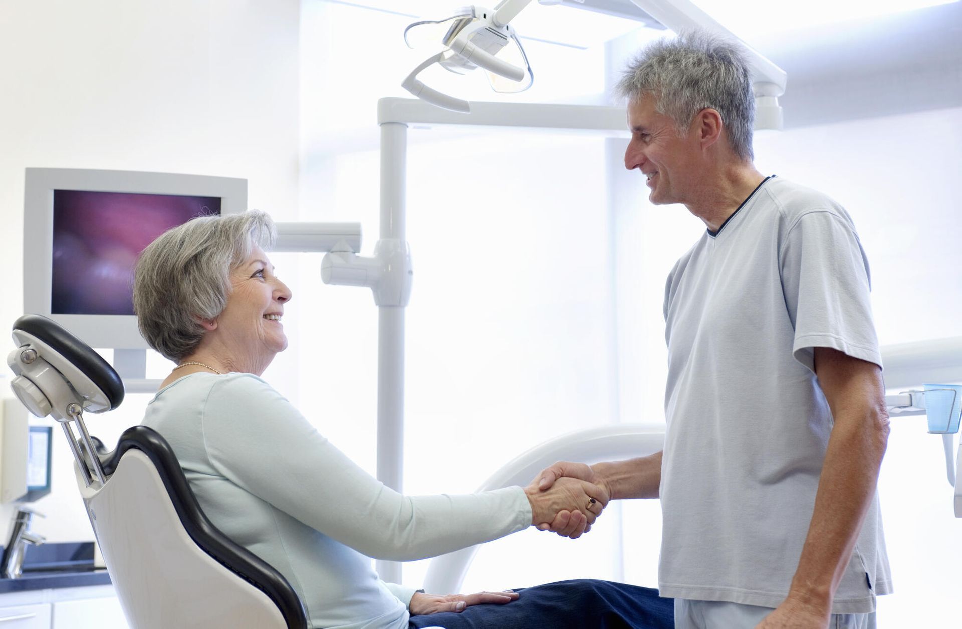 Dentist shaking hands with patient in a dental office. Both are smiling.