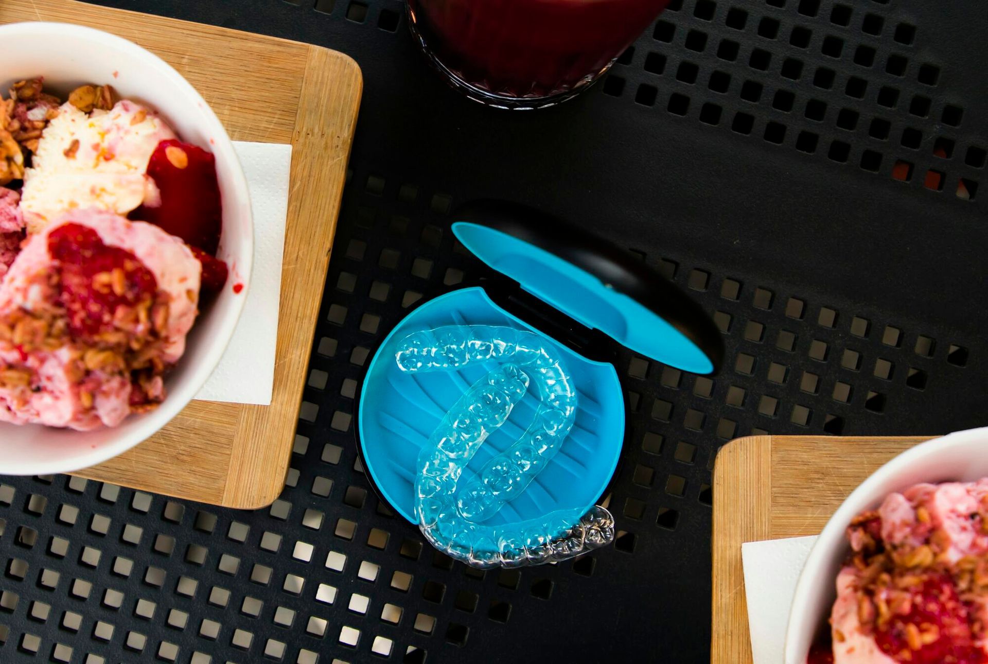 Two bowls of dessert with toppings, a blue coaster, and a beverage on a black table.