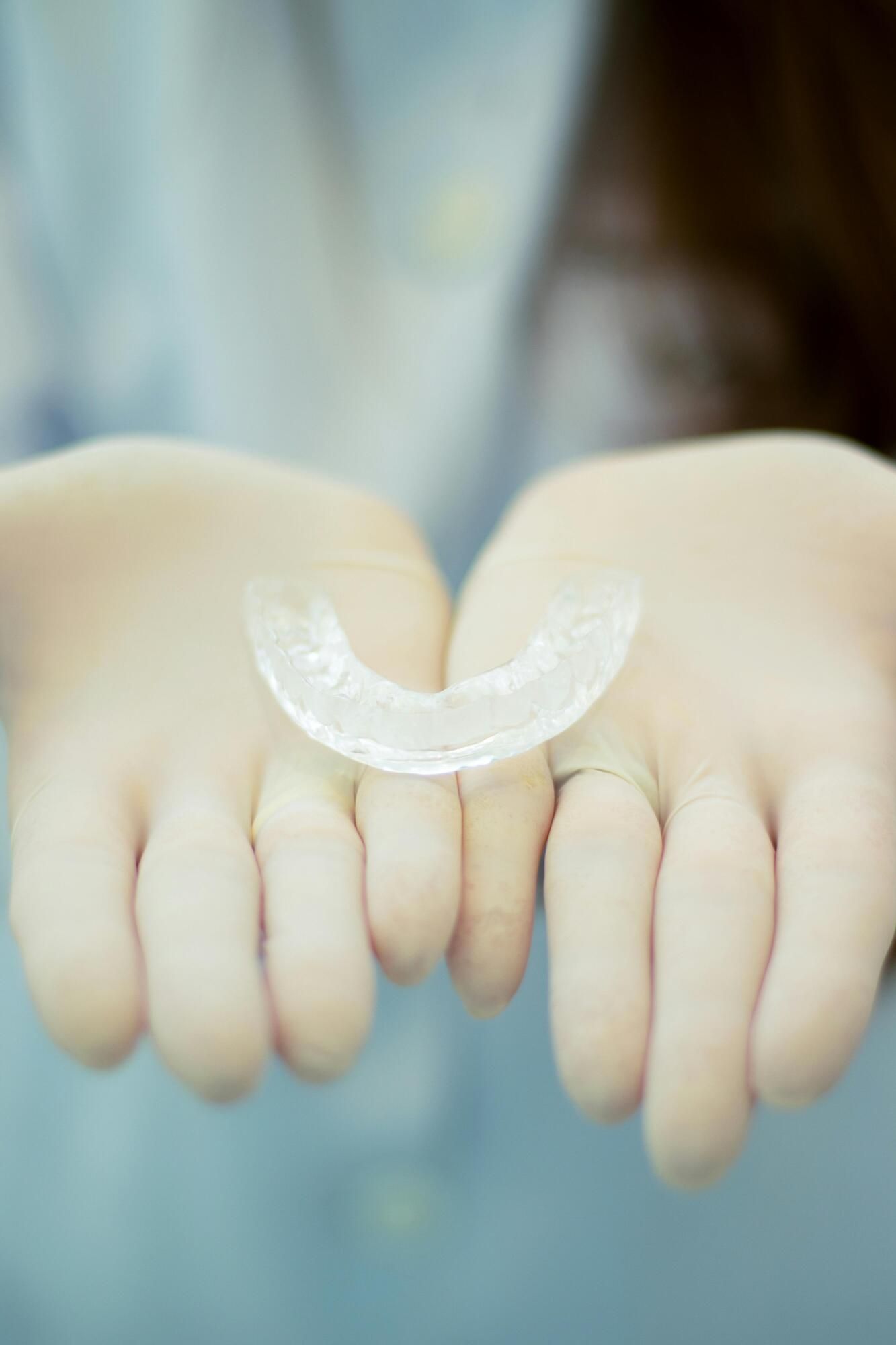 Gloved hands holding a clear, U-shaped dental retainer.