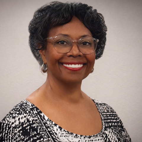Woman wearing glasses, smiling, in a black and white patterned top.