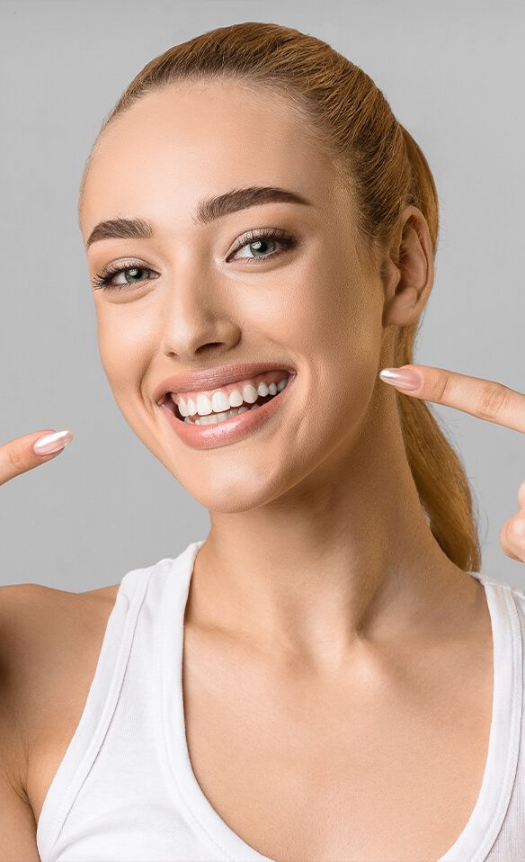 Woman with blond hair smiling, pointing at her white teeth.