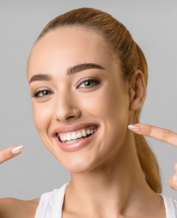 Woman with blonde ponytail smiles, pointing at her teeth.