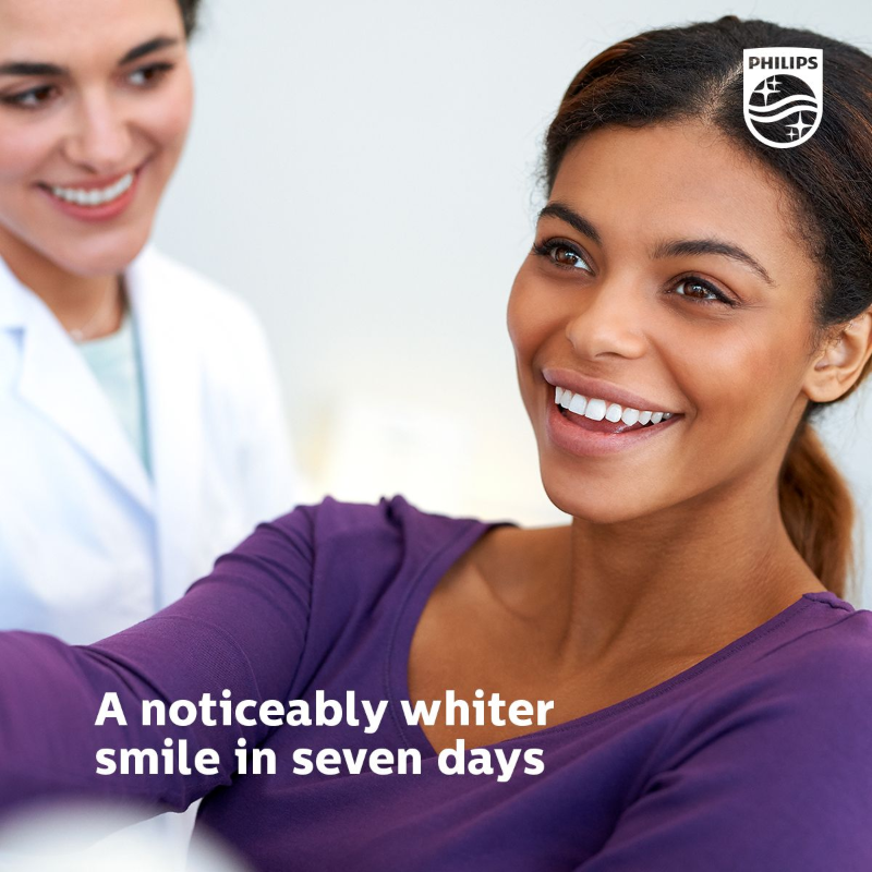 Woman with a bright smile, being observed by a dentist, promoting Philips whitening products. Text: