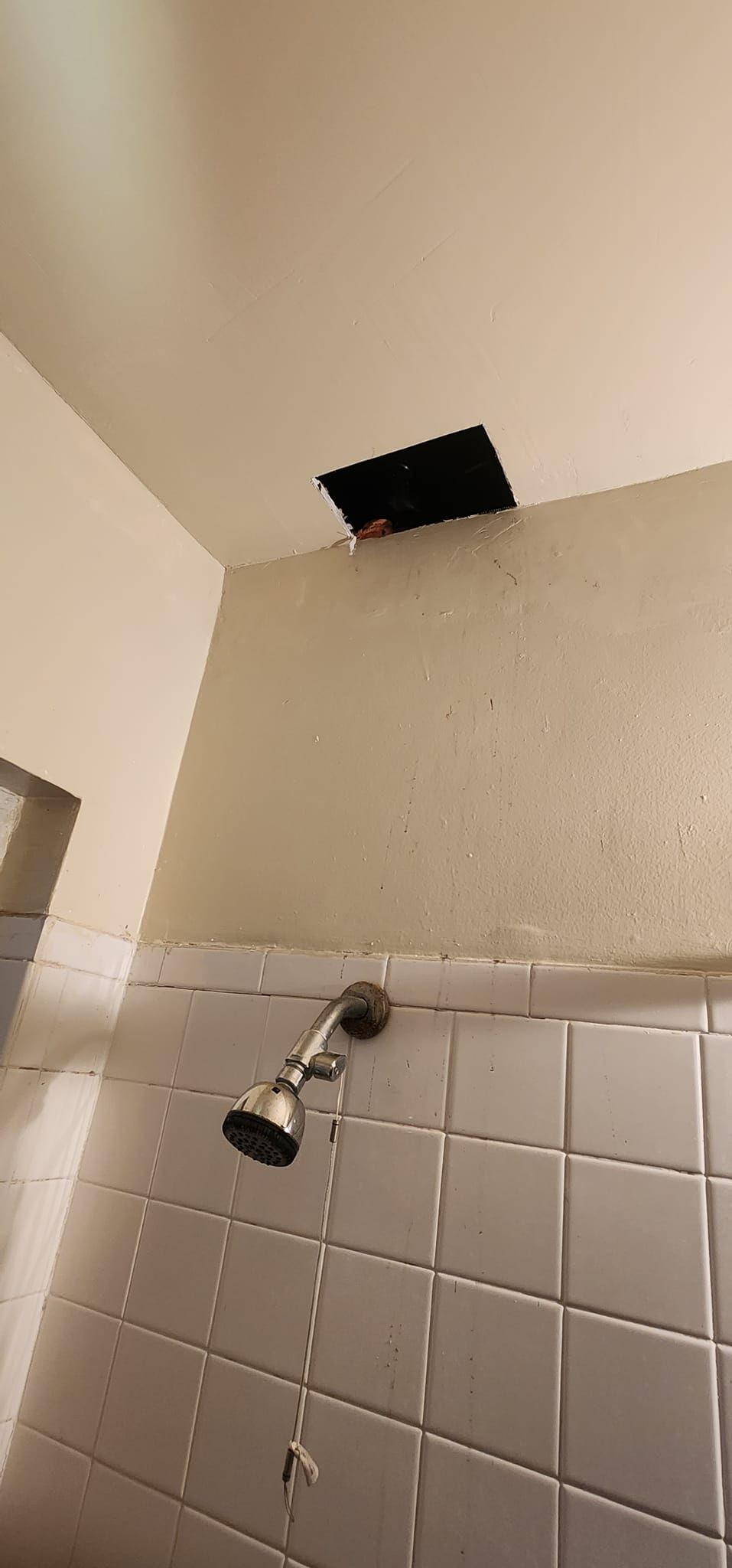 A bathroom with a shower head and a hole in the ceiling.