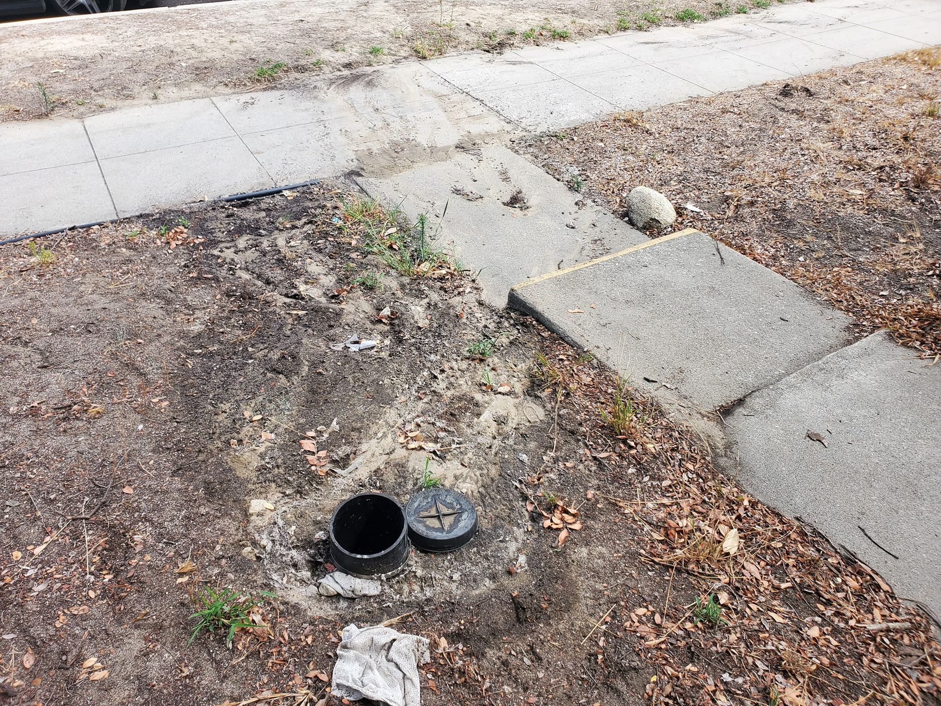 A couple of pots are sitting on the ground next to a sidewalk.