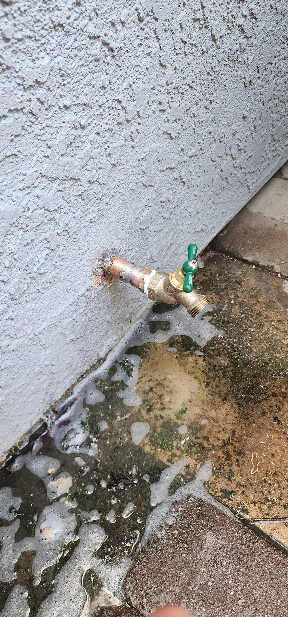 A close up of a faucet on a sidewalk next to a wall.