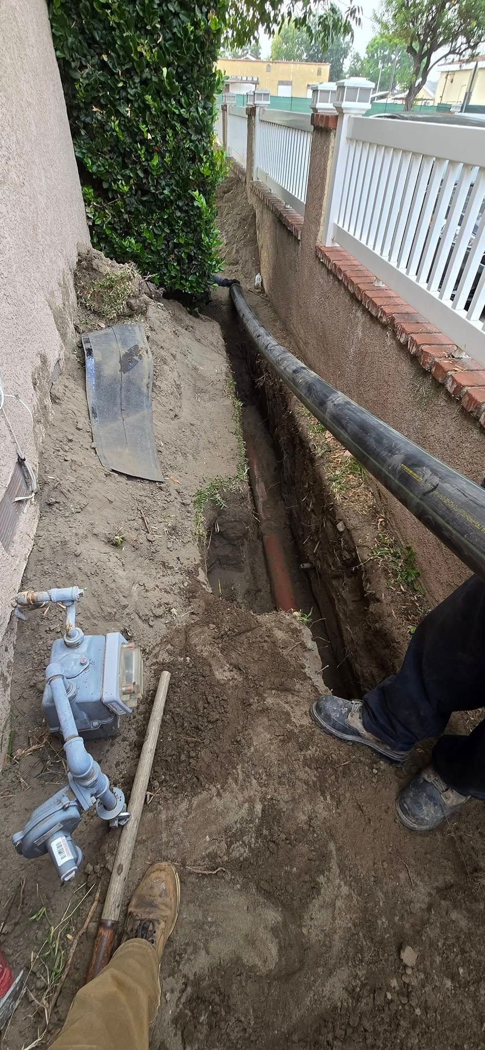 A man is digging a hole in the ground next to a wall.