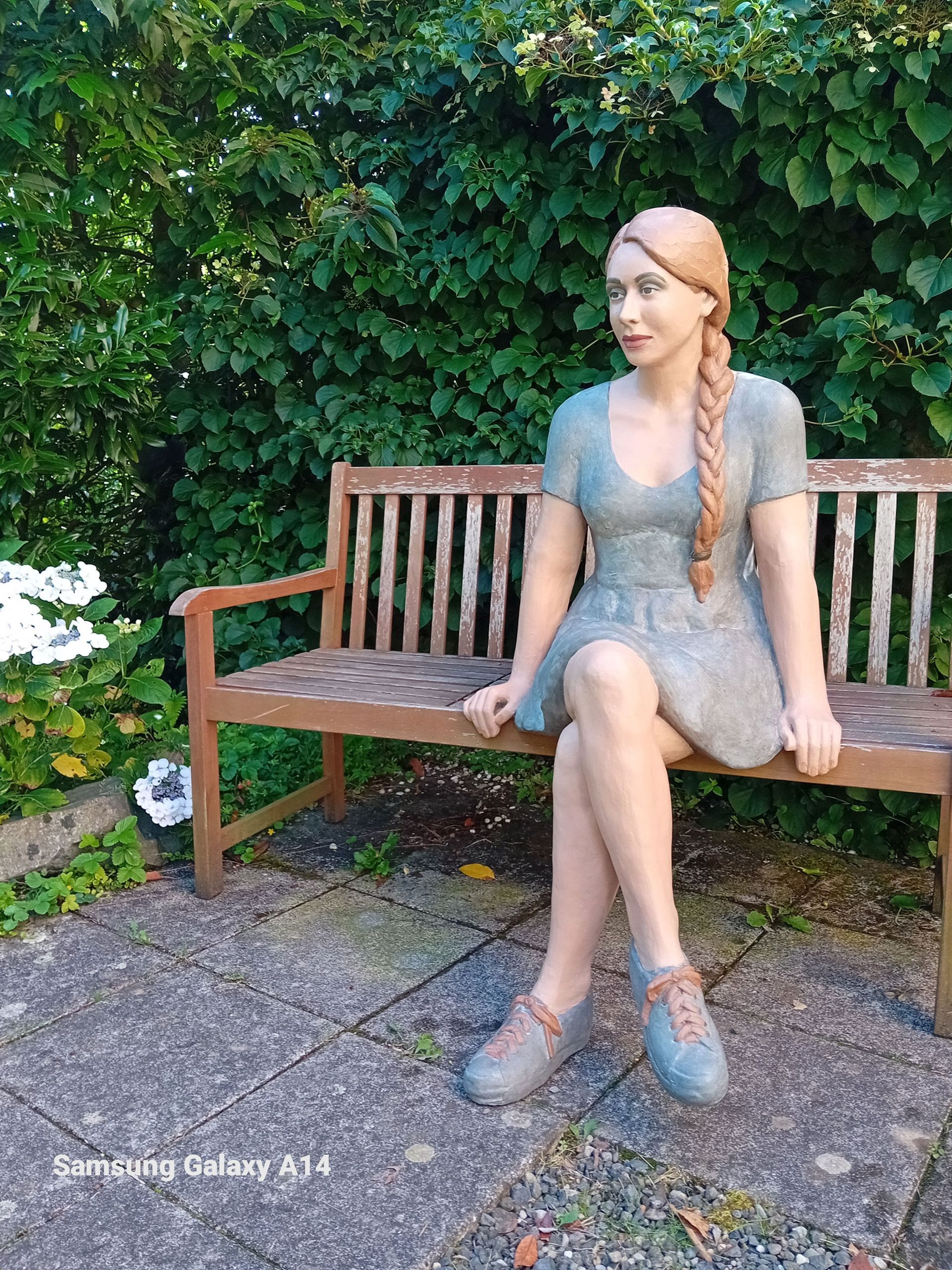 Eine Frauenstatue sitzt auf einer Holzbank.