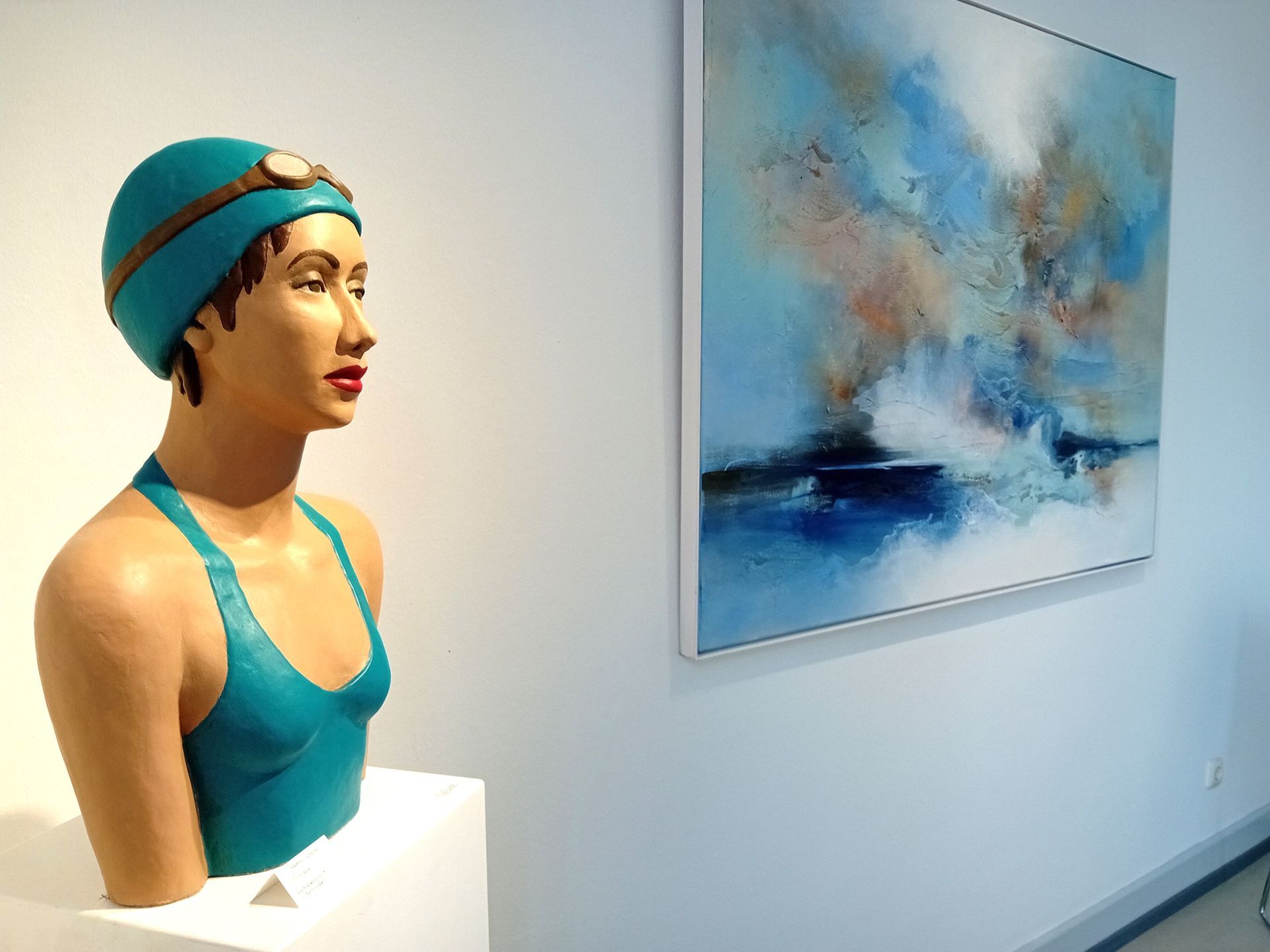 Türkisfarbene Skulptur eines Schwimmers neben einem abstrakten Ozeangemälde.