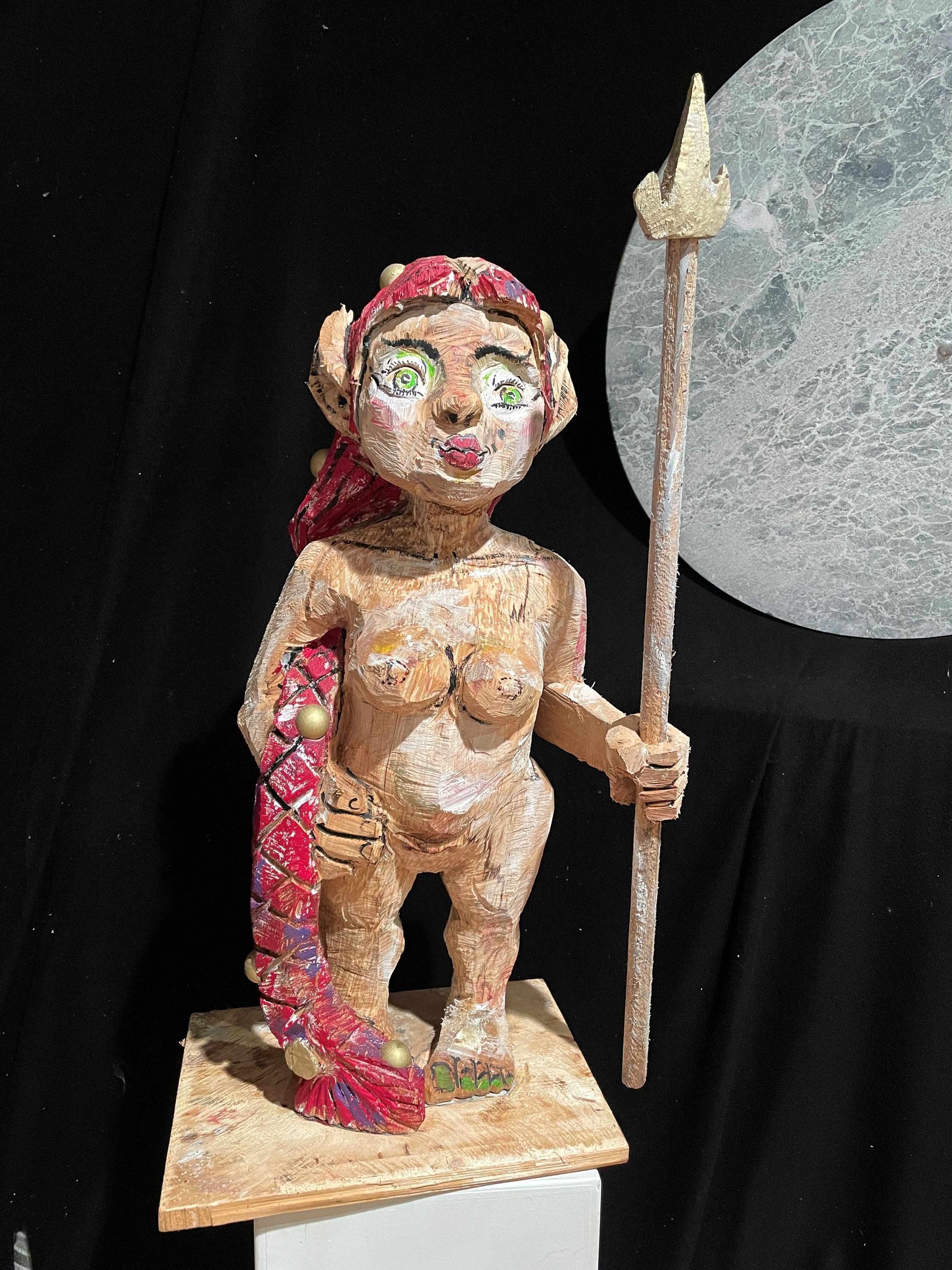 Skulptur einer nackten Figur mit Speer. Rosa Haare, Fischschwanz. Mond im Hintergrund.
