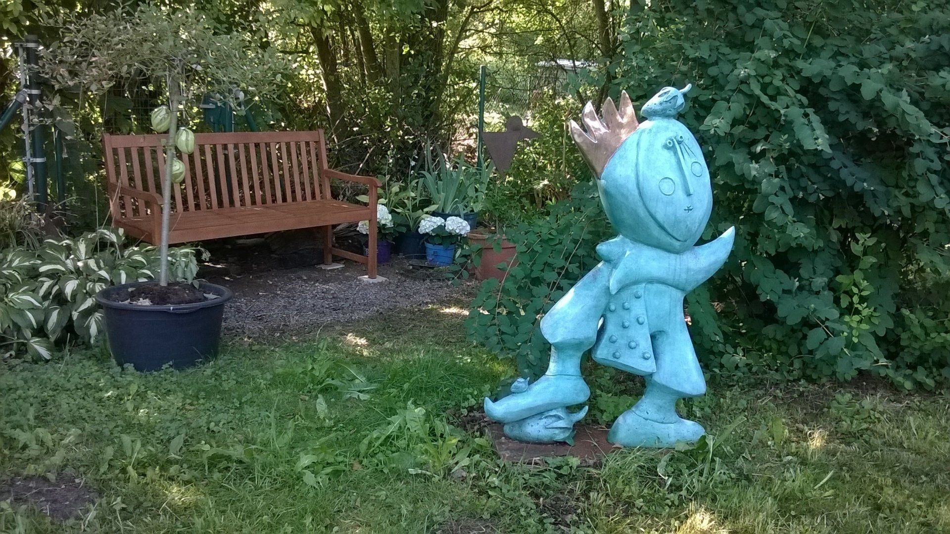 Eine Mickey-Maus-Statue steht im Gras neben einer Bank.