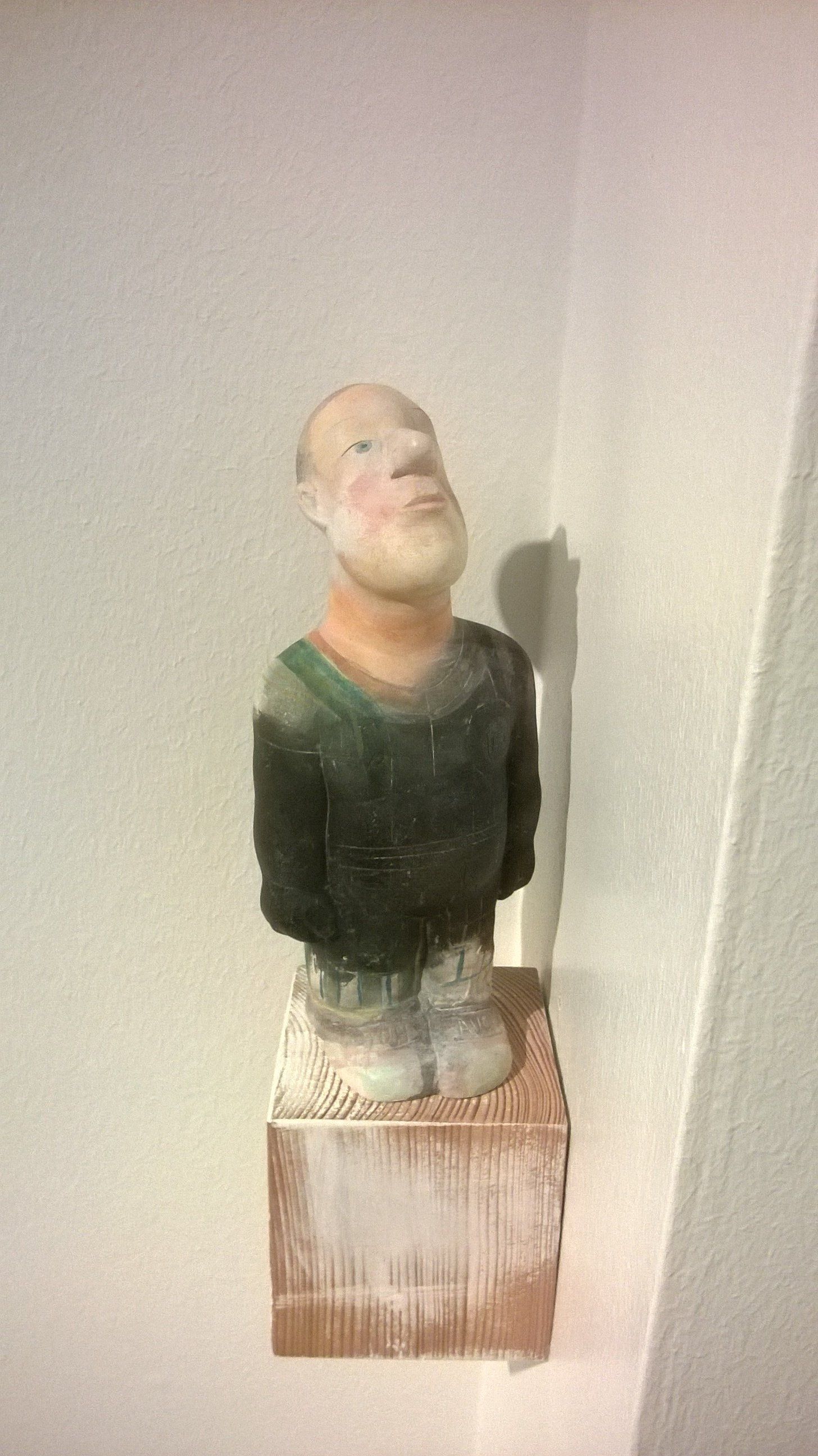 Die Statue eines Mannes mit Bart sitzt auf einem Holzblock.