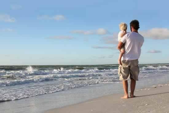 un ragazzo con in braccio un bambino sulla riva del mare