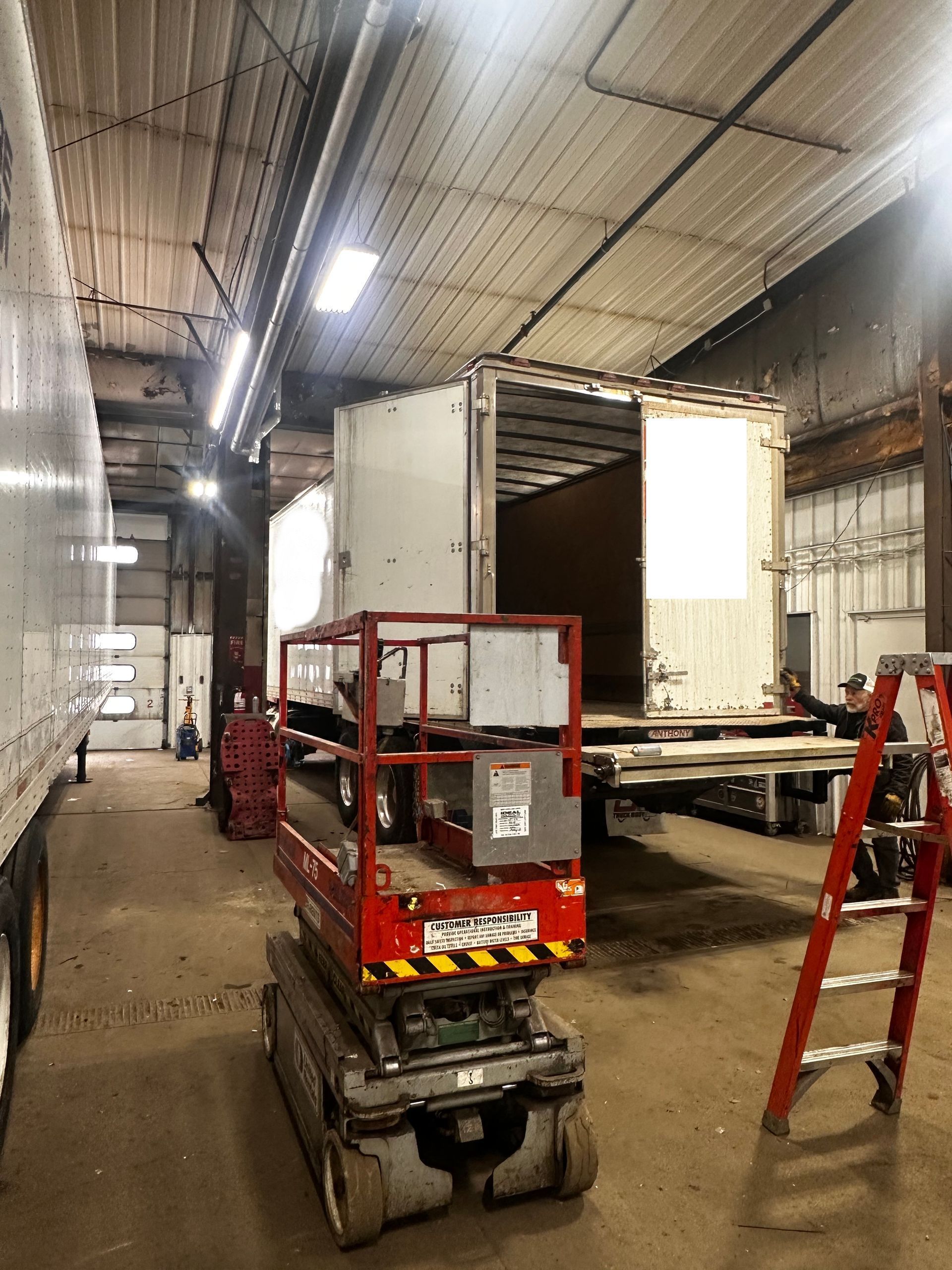 A red scissor lift is sitting in a garage next to a ladder.