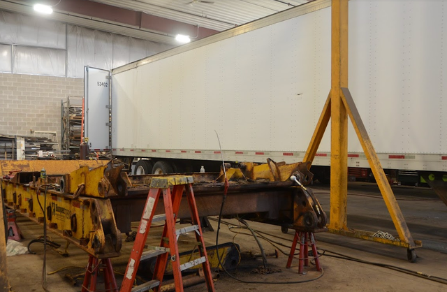 A trailer is being repaired in a garage with a ladder.