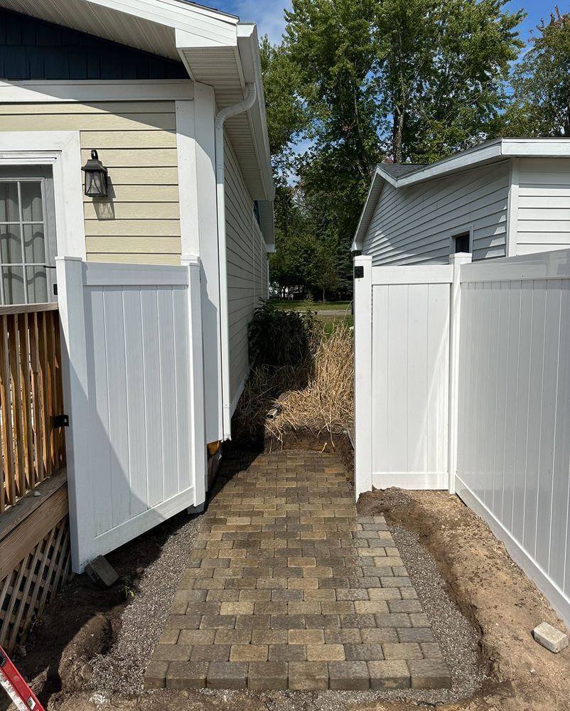 A brick walkway leading to a house with a white fence.