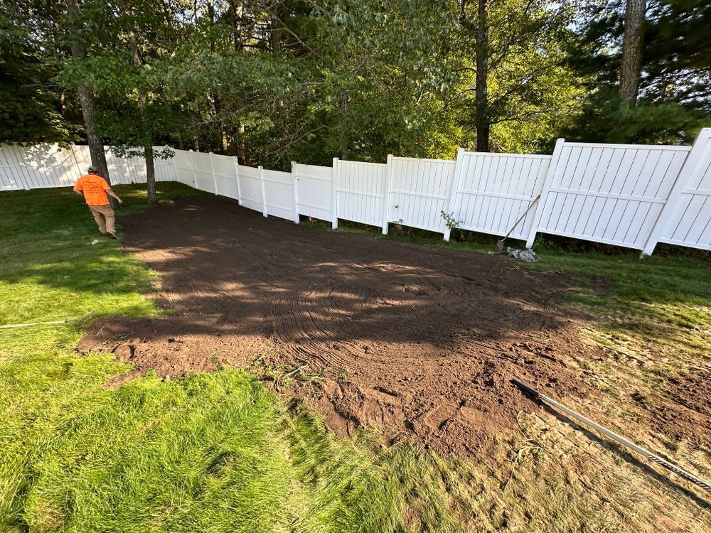 A man is standing in a yard next to a white fence.
