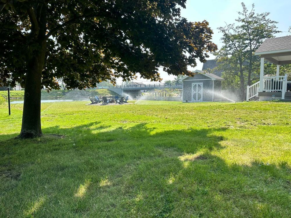 A sprinkler is spraying water on a lush green field in front of a house.