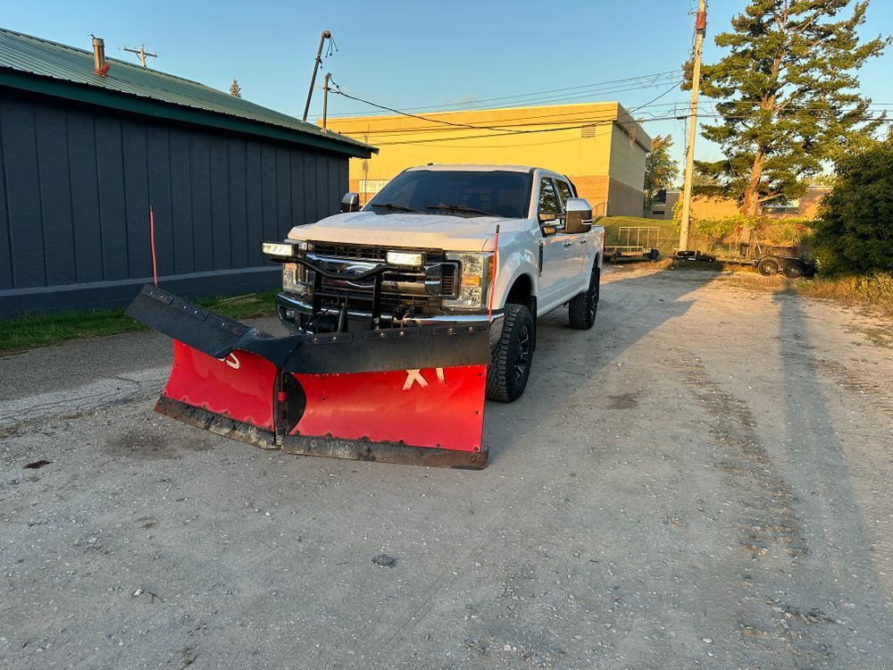 A white truck with a red snow plow on the front is parked in a parking lot.