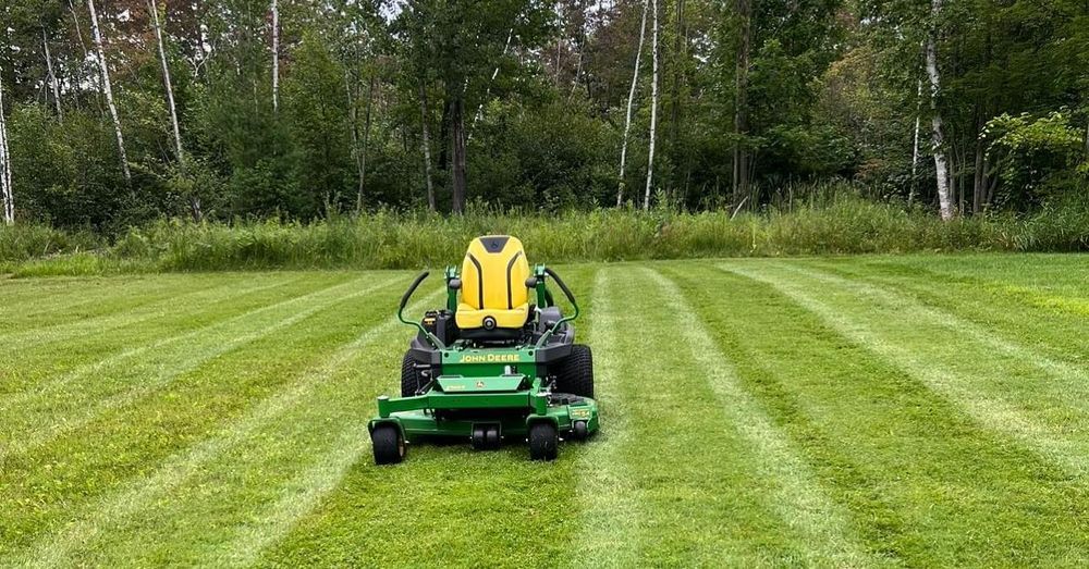 A person is riding a lawn mower through a lush green field.