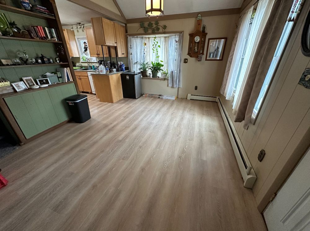 A living room with hardwood floors and a kitchen in the background.
