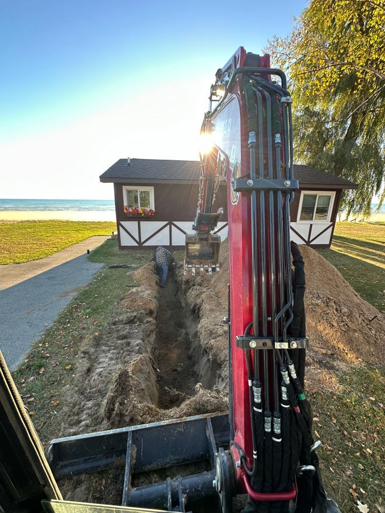 A red excavator is digging a hole in front of a house.