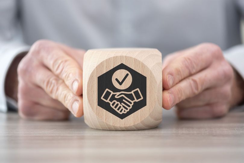 Hands holding a wooden block with a handshake icon and checkmark.