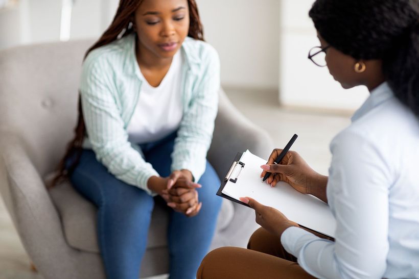 Therapist taking notes during session with a patient seated in a chair.