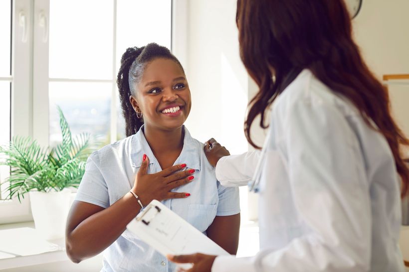 Woman smiles at a doctor in a medical office; doctor has hand on woman’s shoulder.