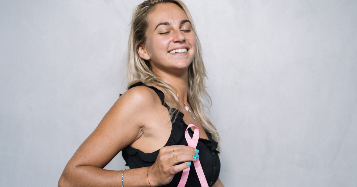 Woman holding pink breast cancer awareness ribbon, smiling.