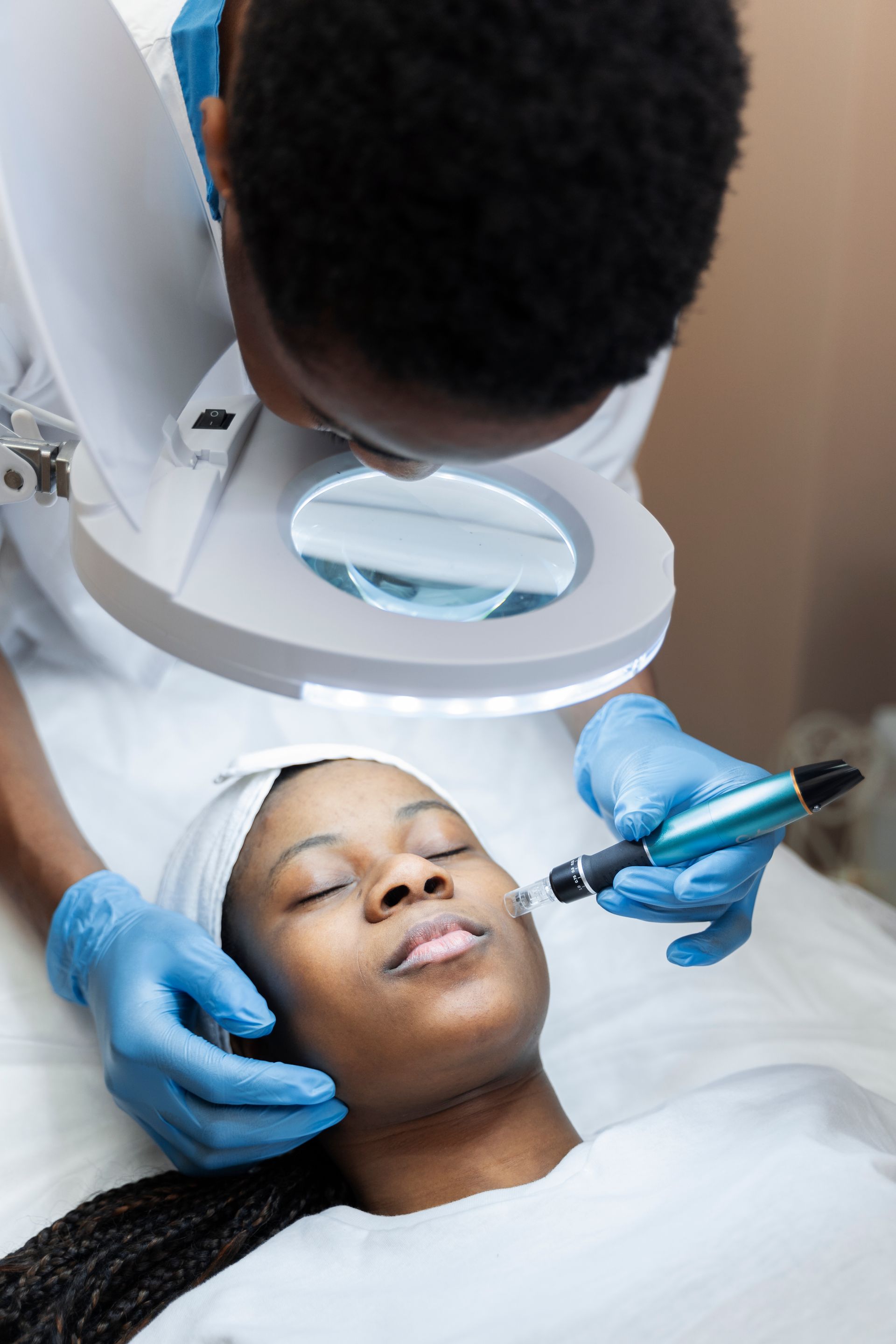 Person receiving cosmetic facial treatment with magnifying lamp.