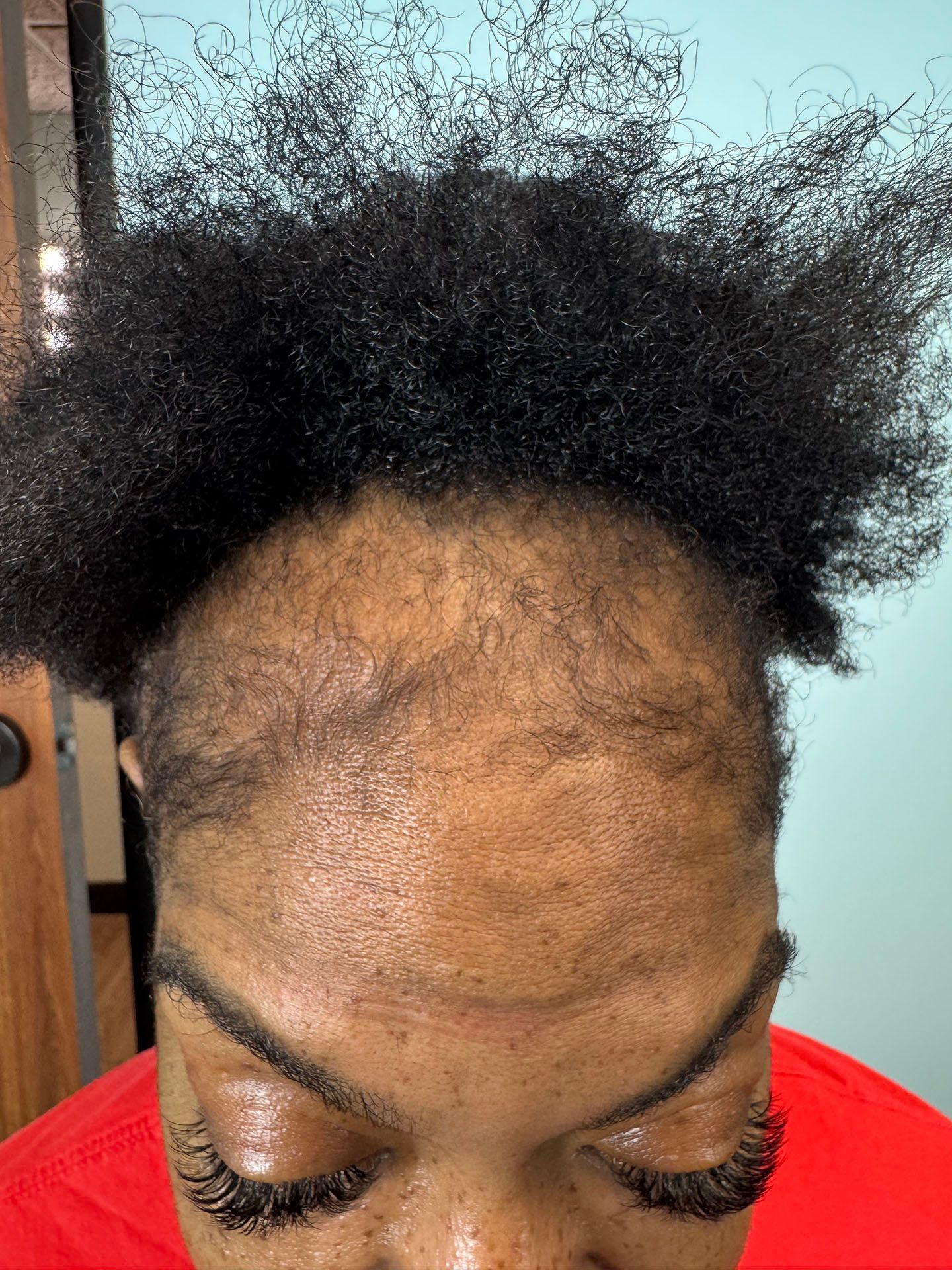 Person with dark, textured hair and visible hairline; wearing a red shirt, eyes closed.