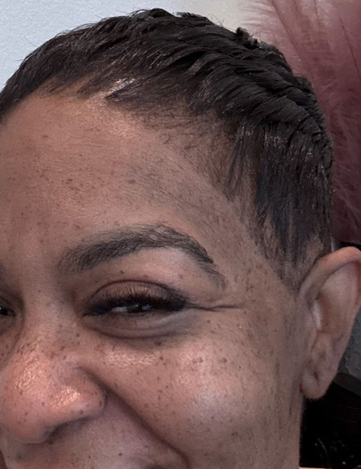 Close-up of a person with short, dark hair, smiling and showing freckled skin. One eyebrow is visible.