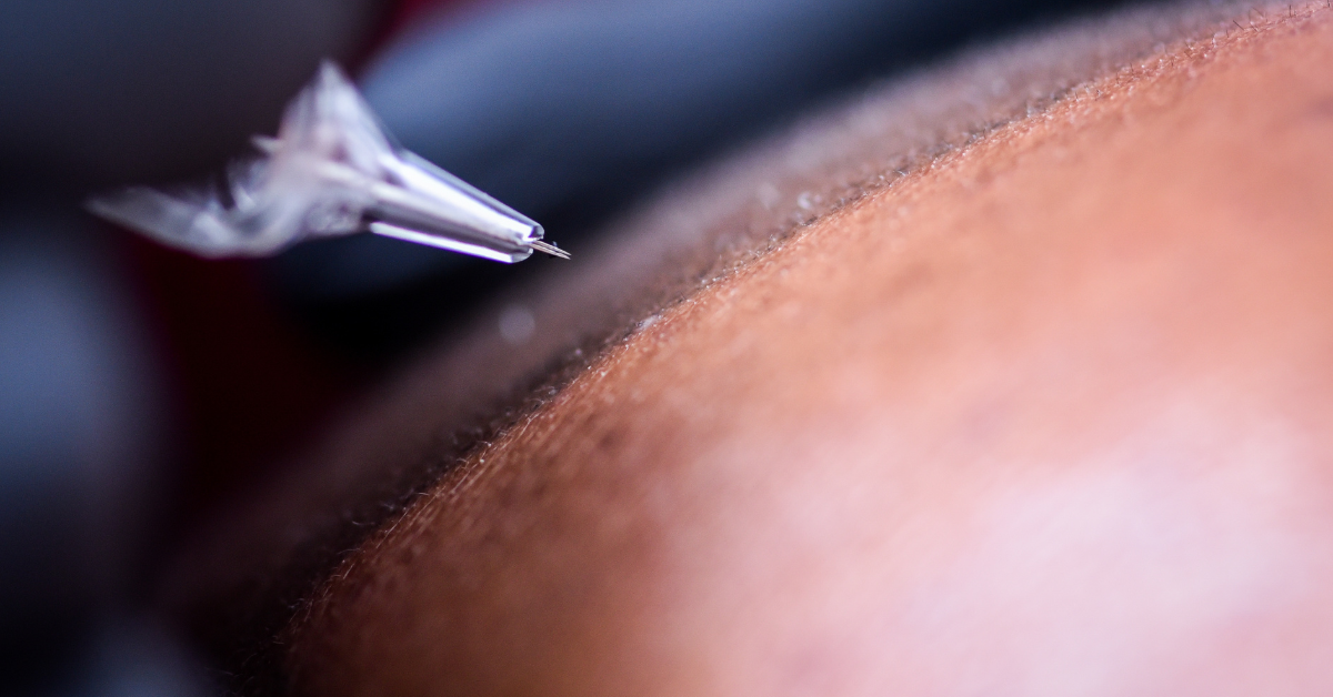 Tattoo machine needle near skin, focused. Blurred background.
