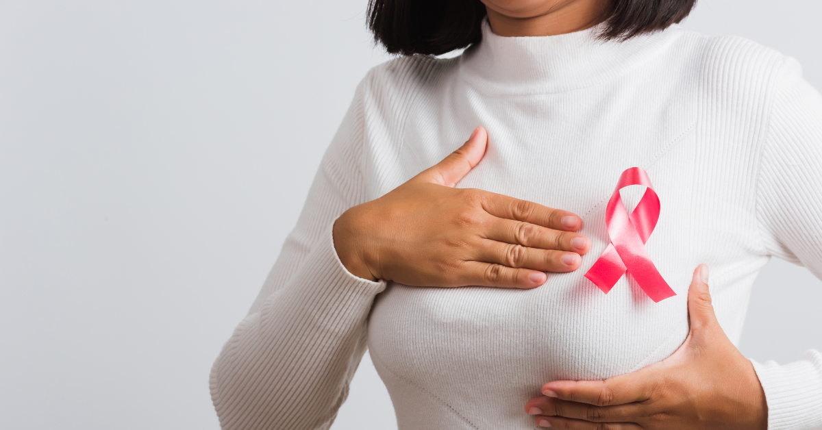 Woman with pink ribbon pinned to chest, hand on breast.