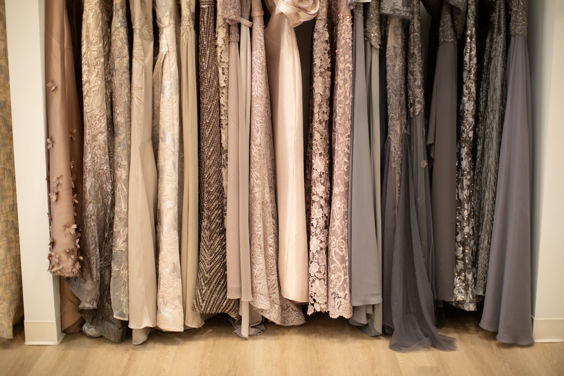 Row of sequined and solid-colored formal dresses hanging in a boutique, varying shades of beige, gray, and brown.
