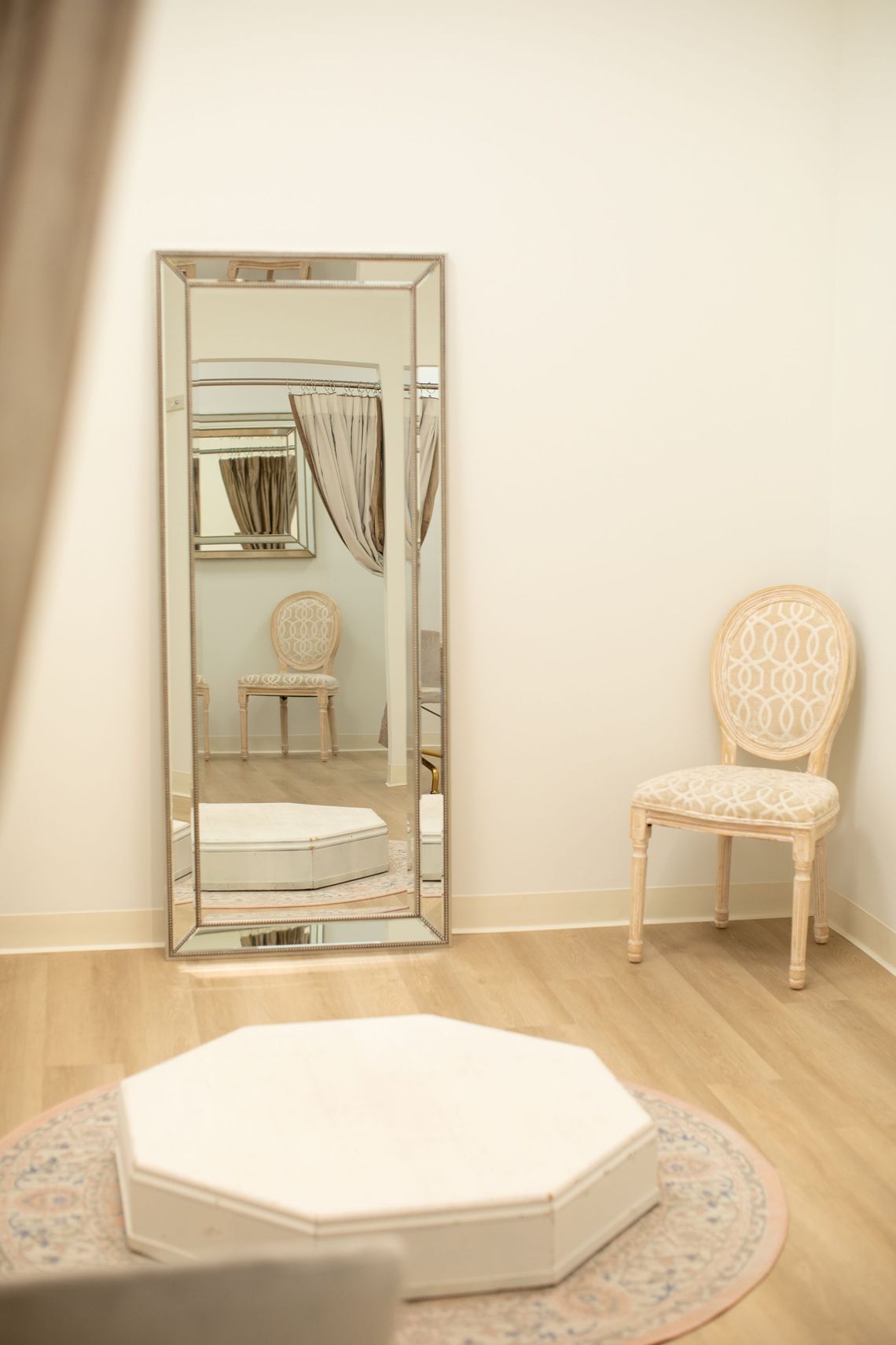 Full-length mirror in a room with a chair, octagonal ottoman, and floral rug.