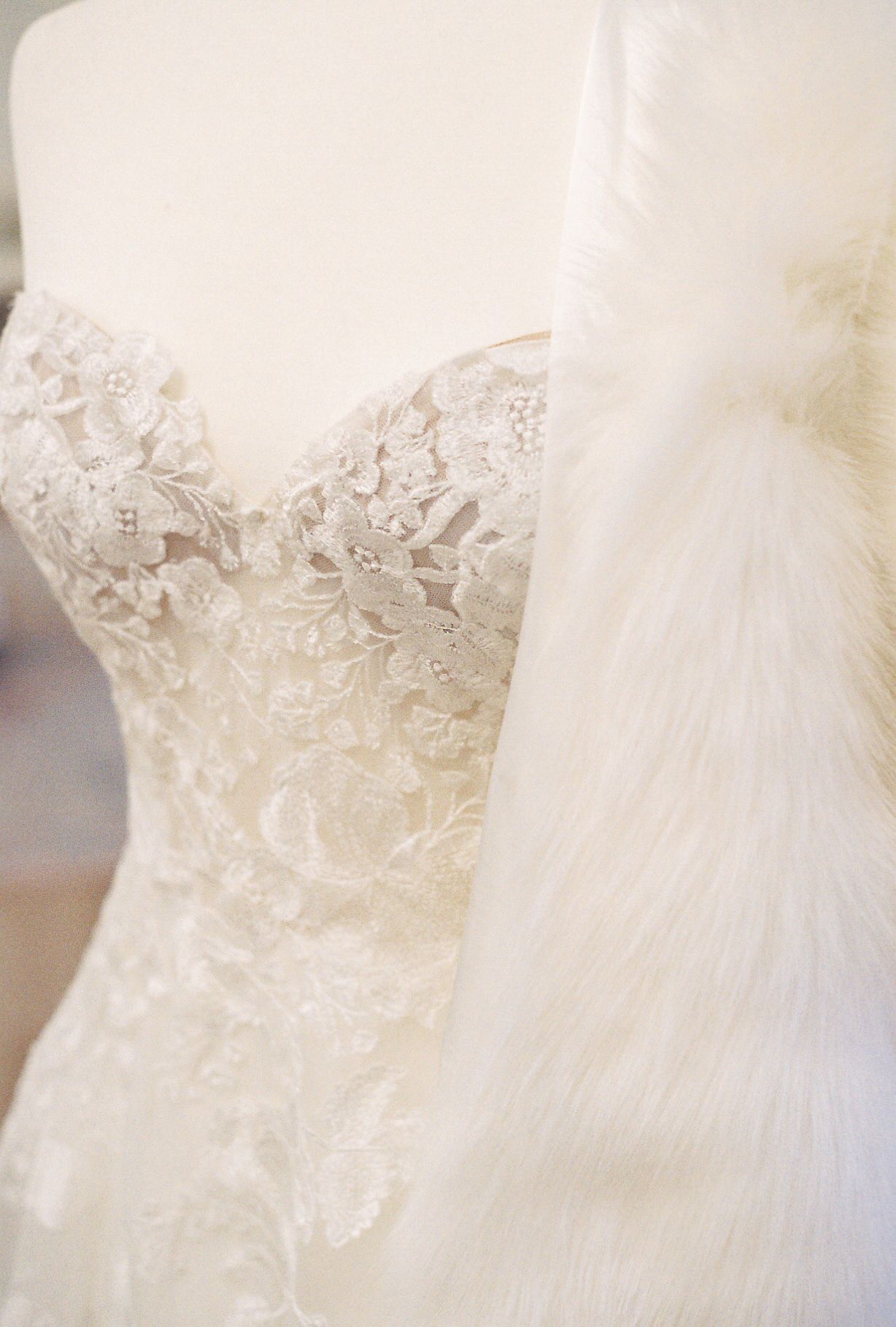 Ivory lace wedding dress on a mannequin, with a white fur wrap draped over it.