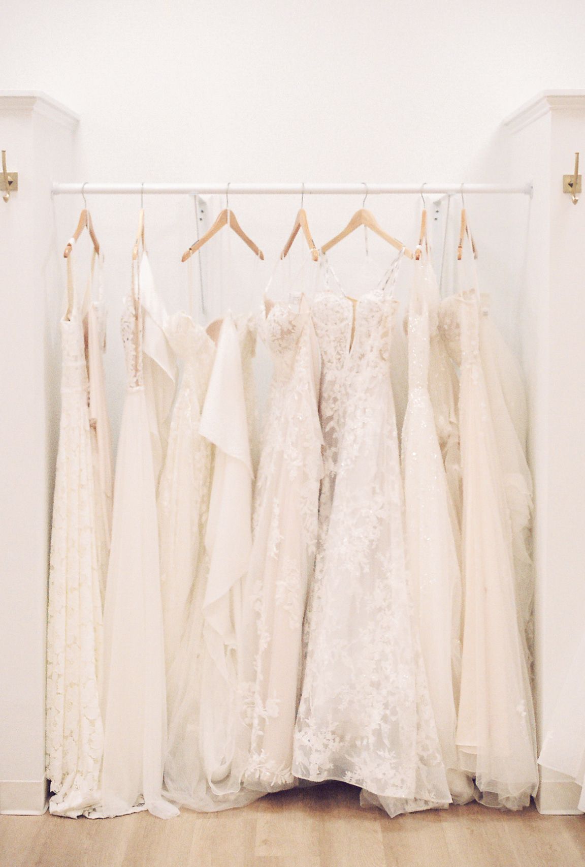 Wedding dresses hanging on a rack in a bright white bridal shop.