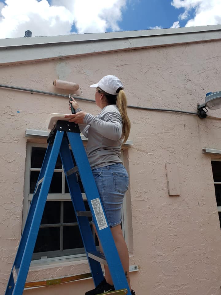 A woman is standing on a ladder painting a building.