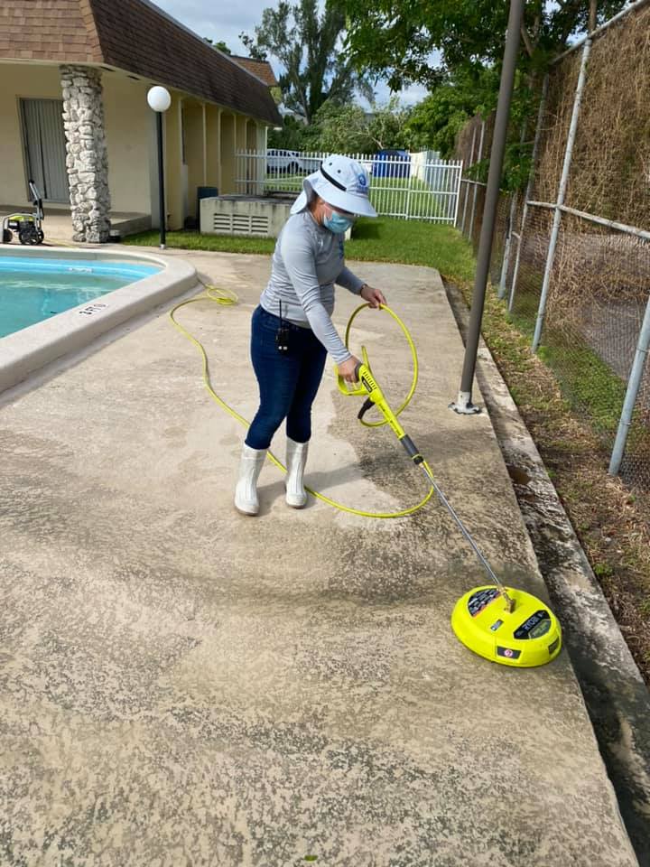 A woman is cleaning the sidewalk next to a pool.