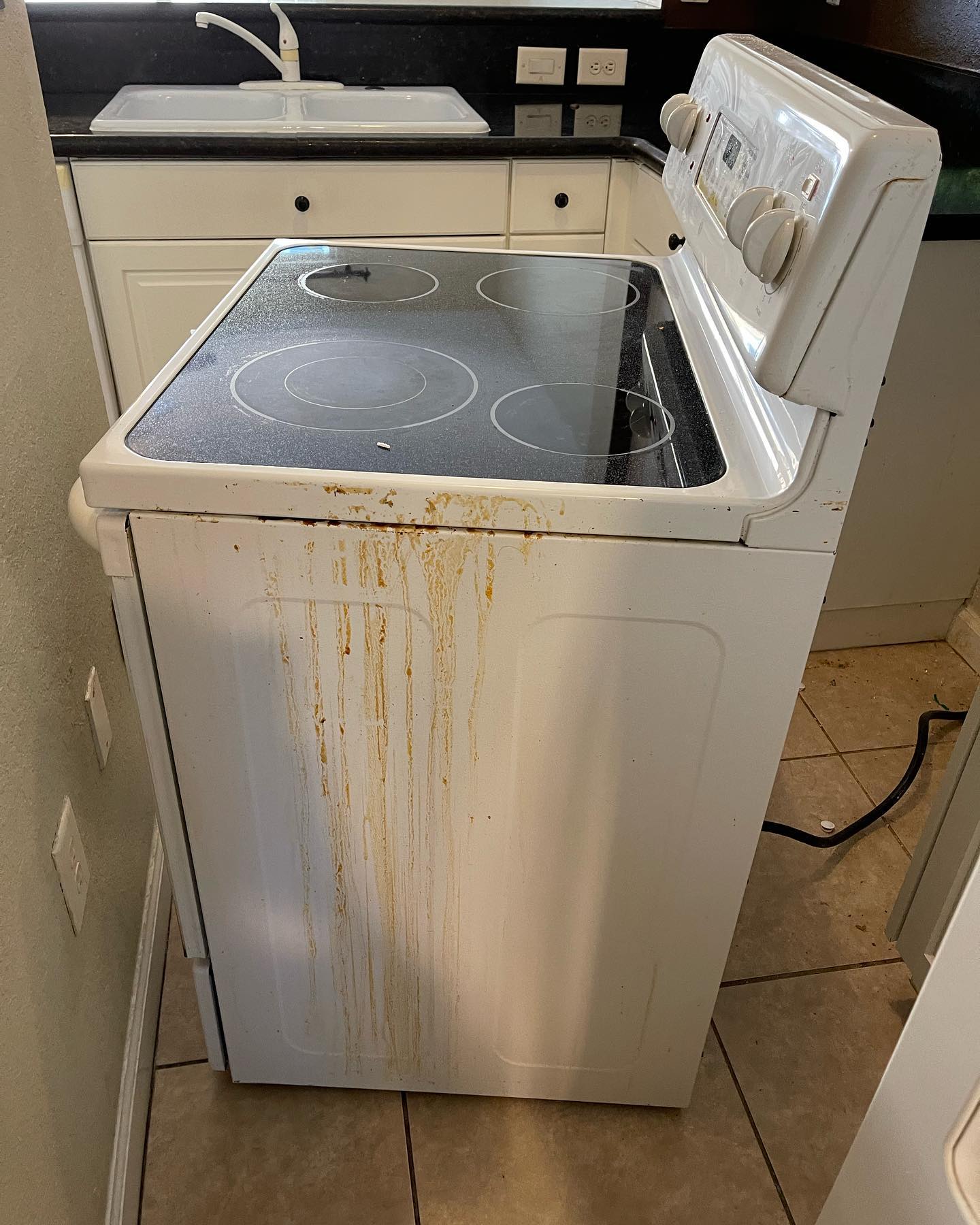 A dirty stove top oven is sitting in a kitchen next to a sink.