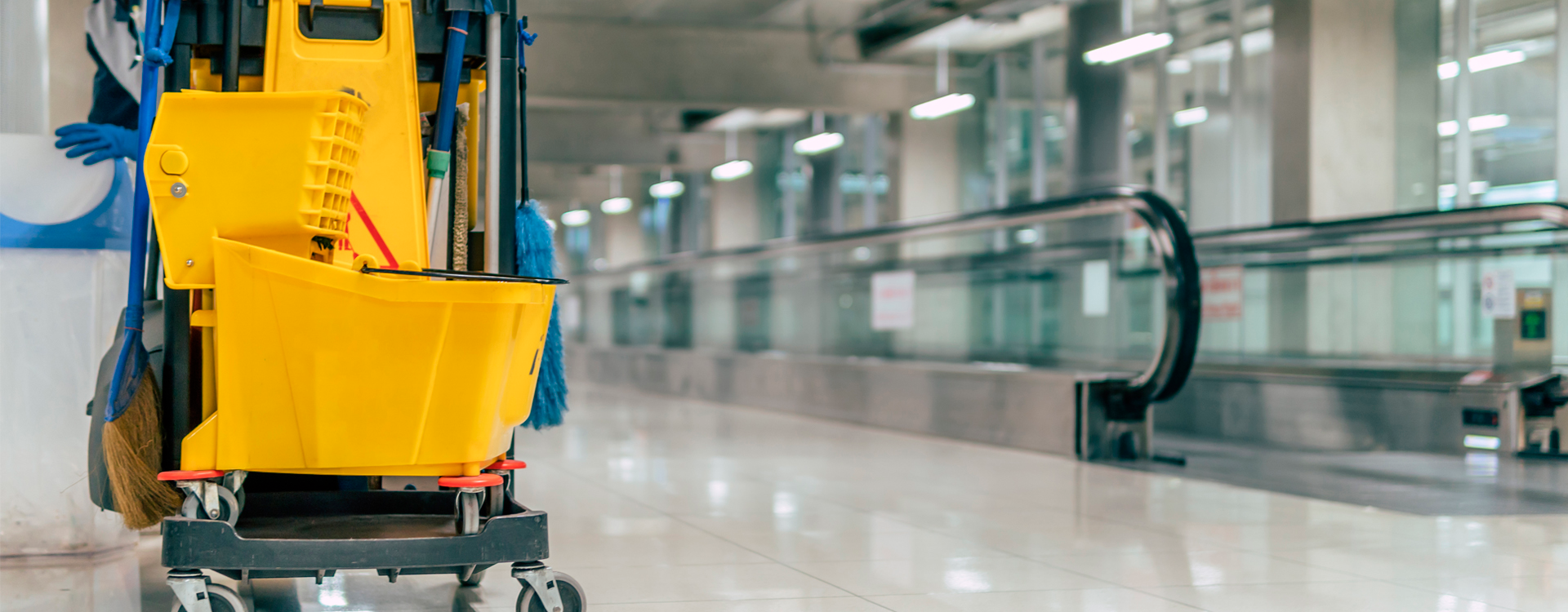 A person is cleaning the floor of a building with a yellow mop and bucket.