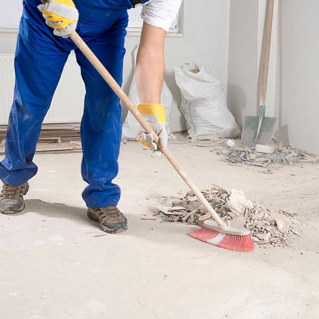 A man in blue overalls is sweeping the floor with a broom.