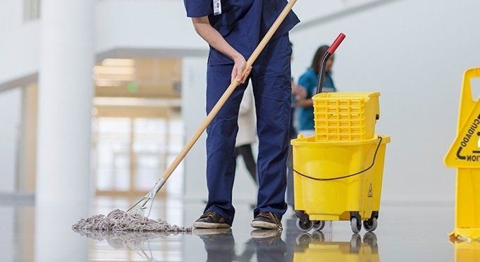 A nurse is mopping the floor of a hospital with a mop.