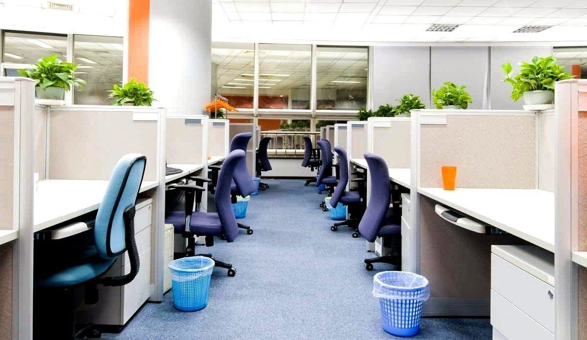 A row of cubicles in an office with a trash can in the middle